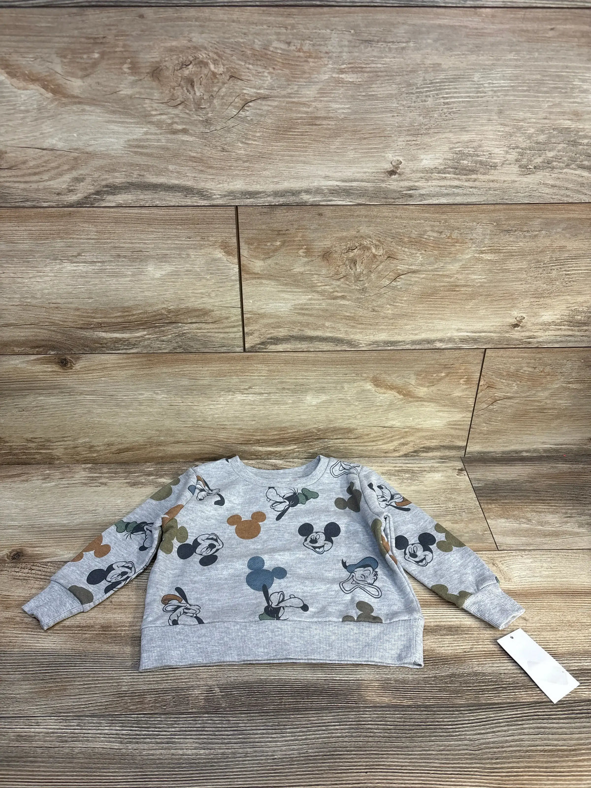 Gray long-sleeve toddler sweatshirt with cartoon character faces and tag on wood background