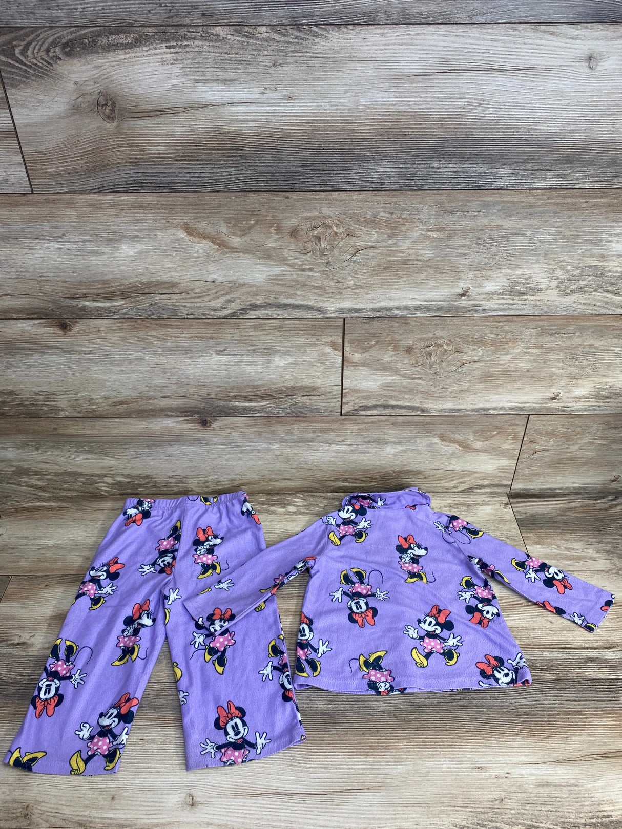 Purple toddler pajama set with Minnie Mouse print, featuring long sleeves and pants on wood floor