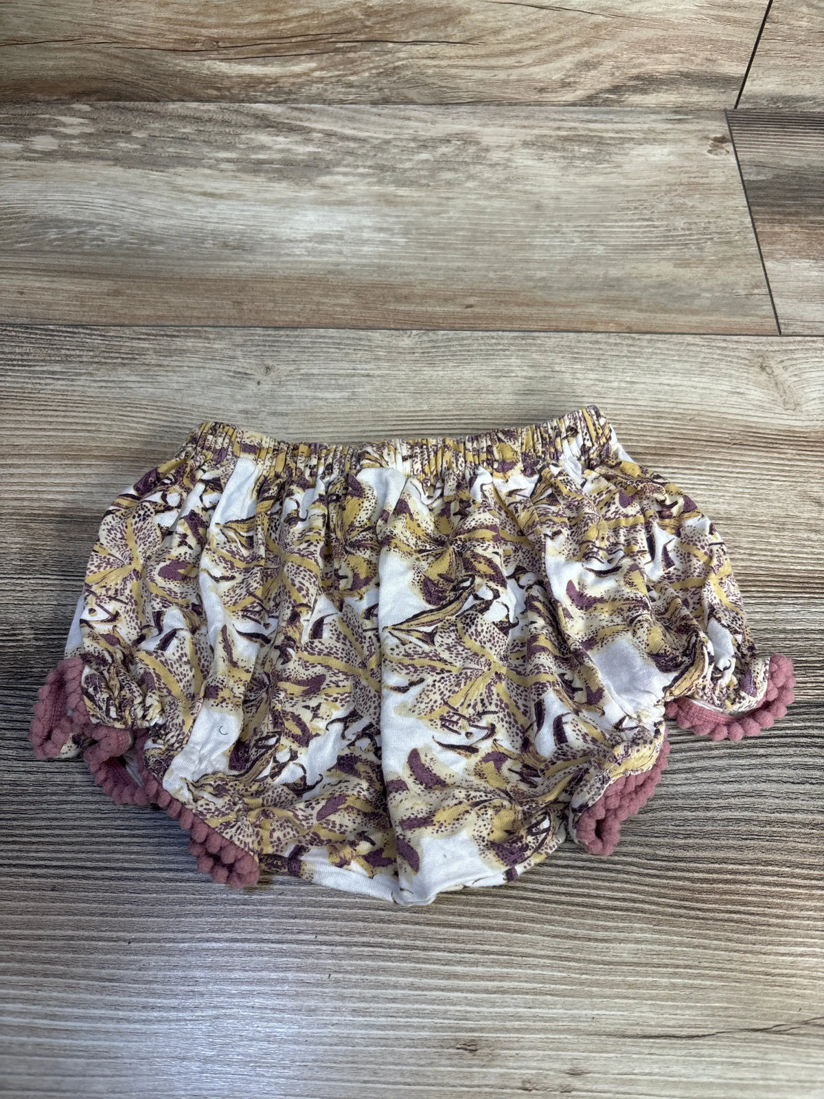 Front view of Kate Quinn bamboo pom-pom bloomers showcasing yellow fabric and pom-pom trim on a wood floor