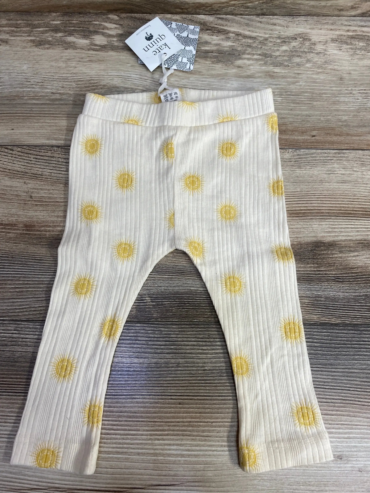 White ribbed baby leggings with yellow sun patterns on wooden floor, Kate Quinn tag attached