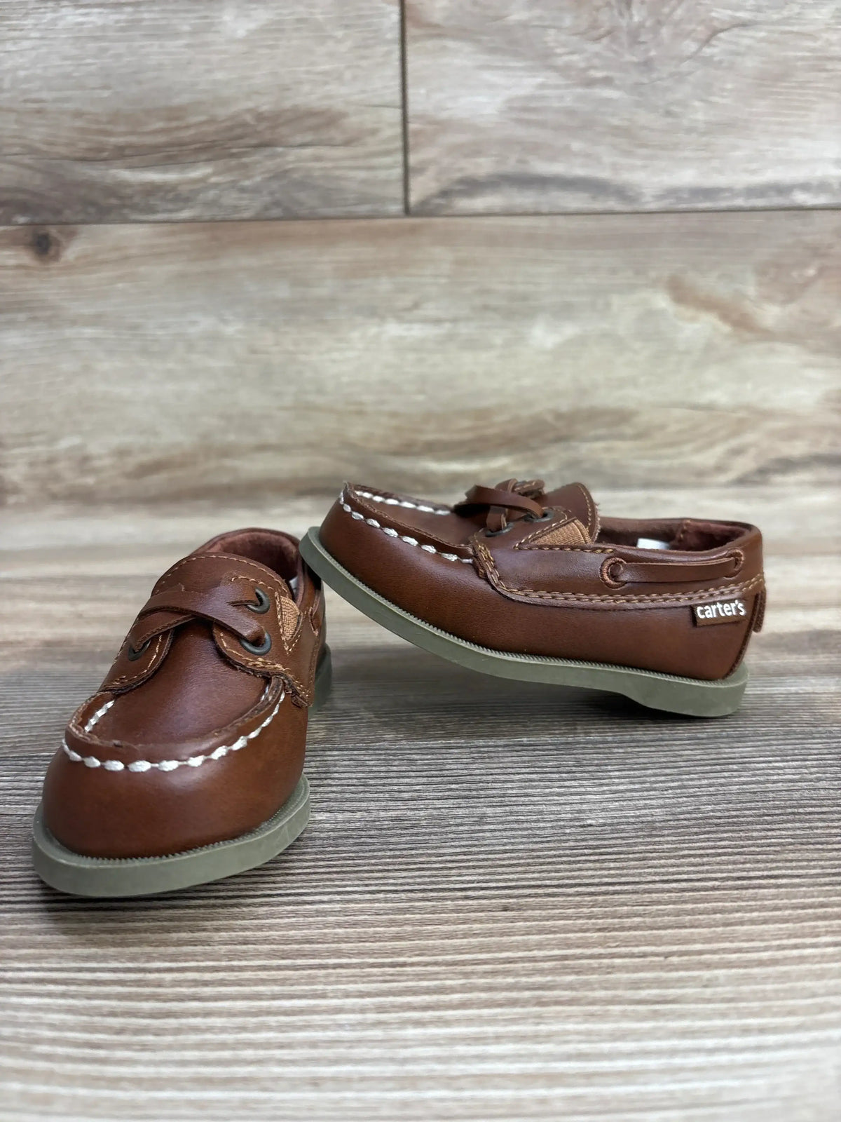 Pair of brown toddler boat shoes by Carter's with white stitching on wood surface