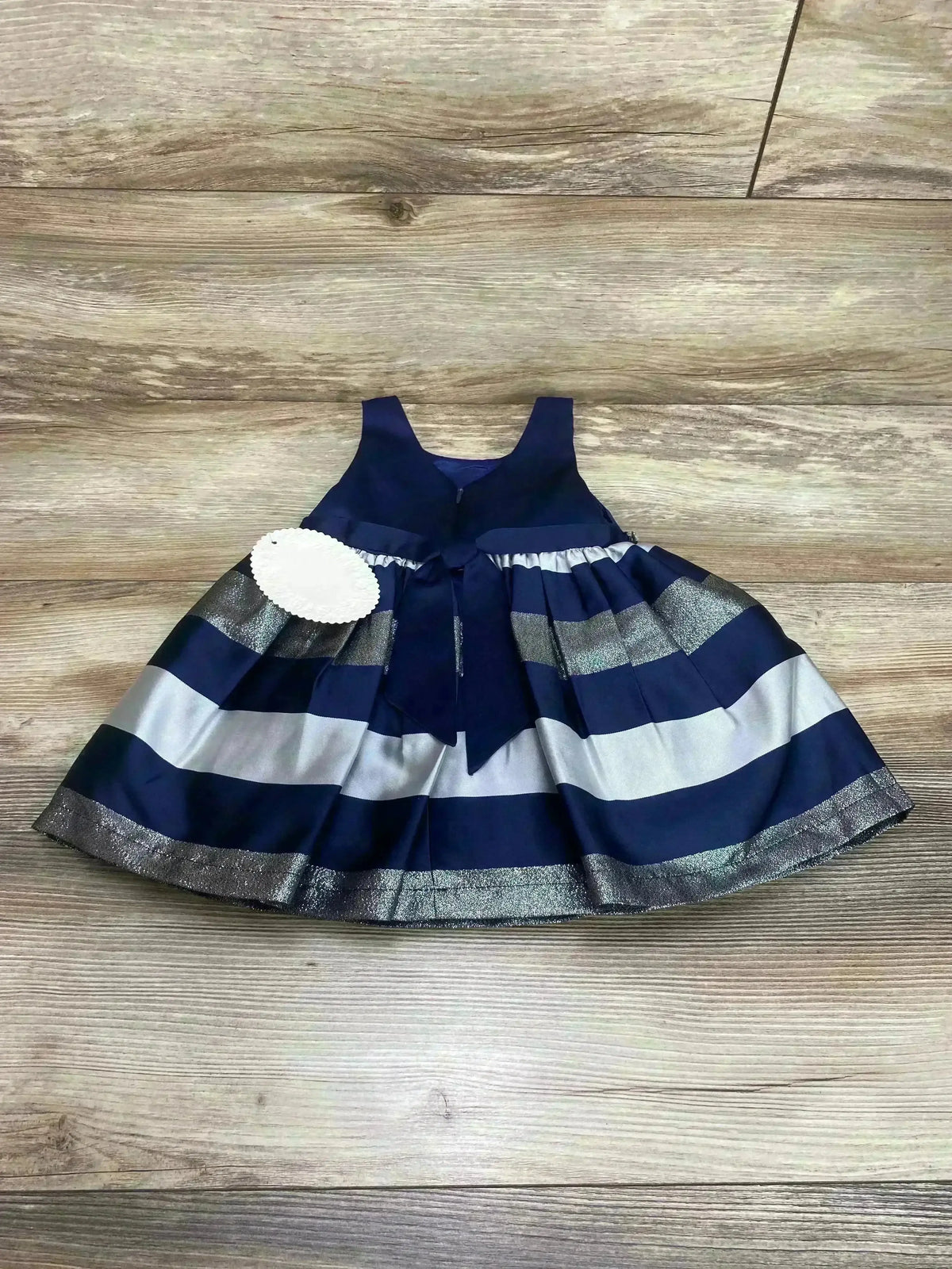 Flat-lay of navy and silver striped sleeveless toddler dress showcasing bow at waist and pleated skirt on wood floor
