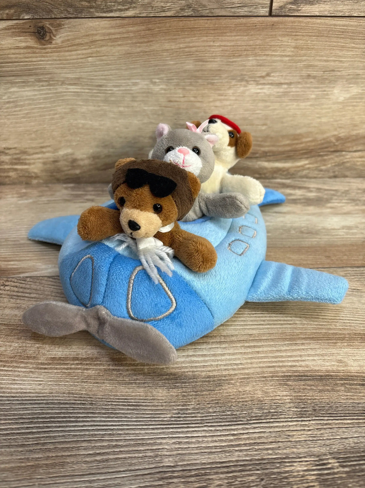 Three-quarter view of Unipak plush blue airplane with three attached finger puppets on wood