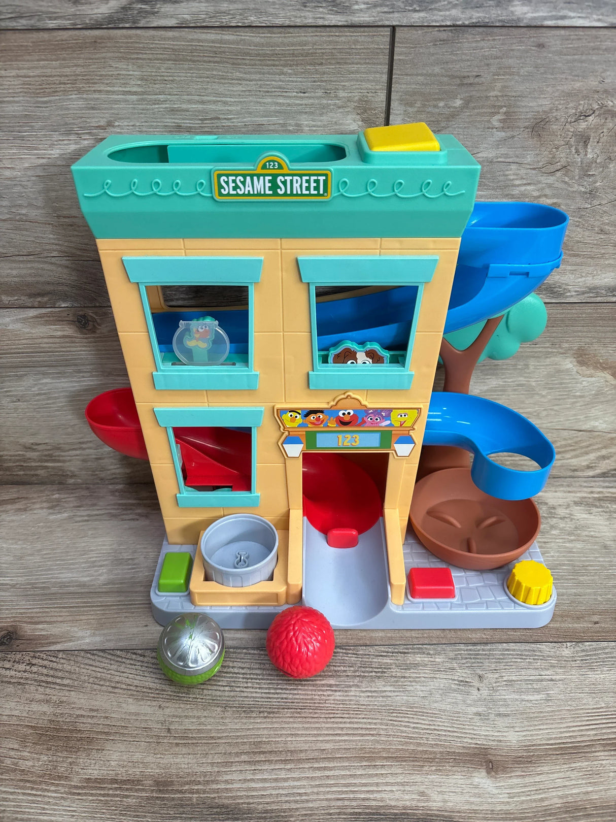 Sesame Street playset toy with building façade, slides, and character balls on wood floor