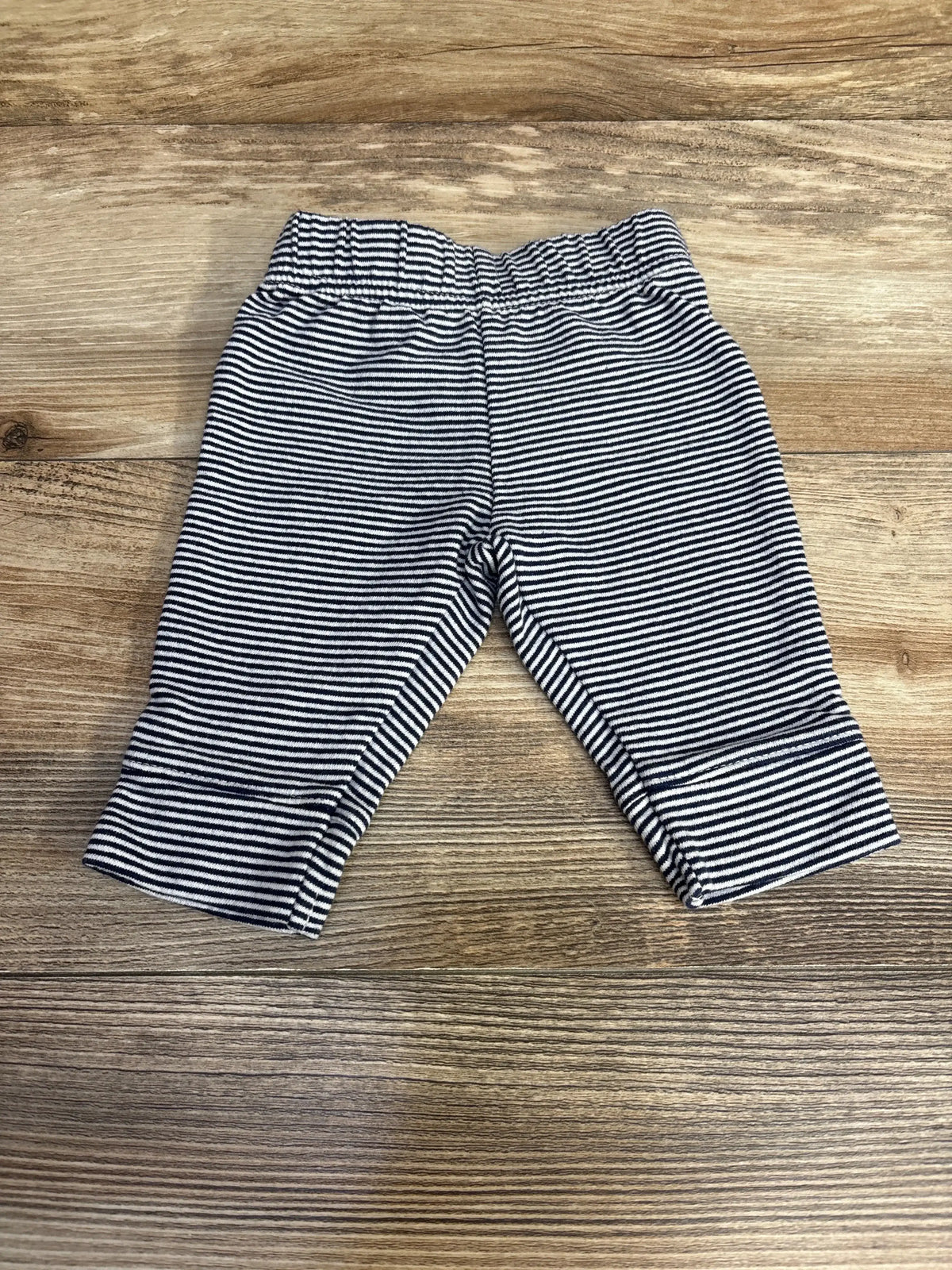 Flat lay of Carter’s navy and white striped baby pants, size 3 months, elastic waistband and cuffed ankles on light wood background