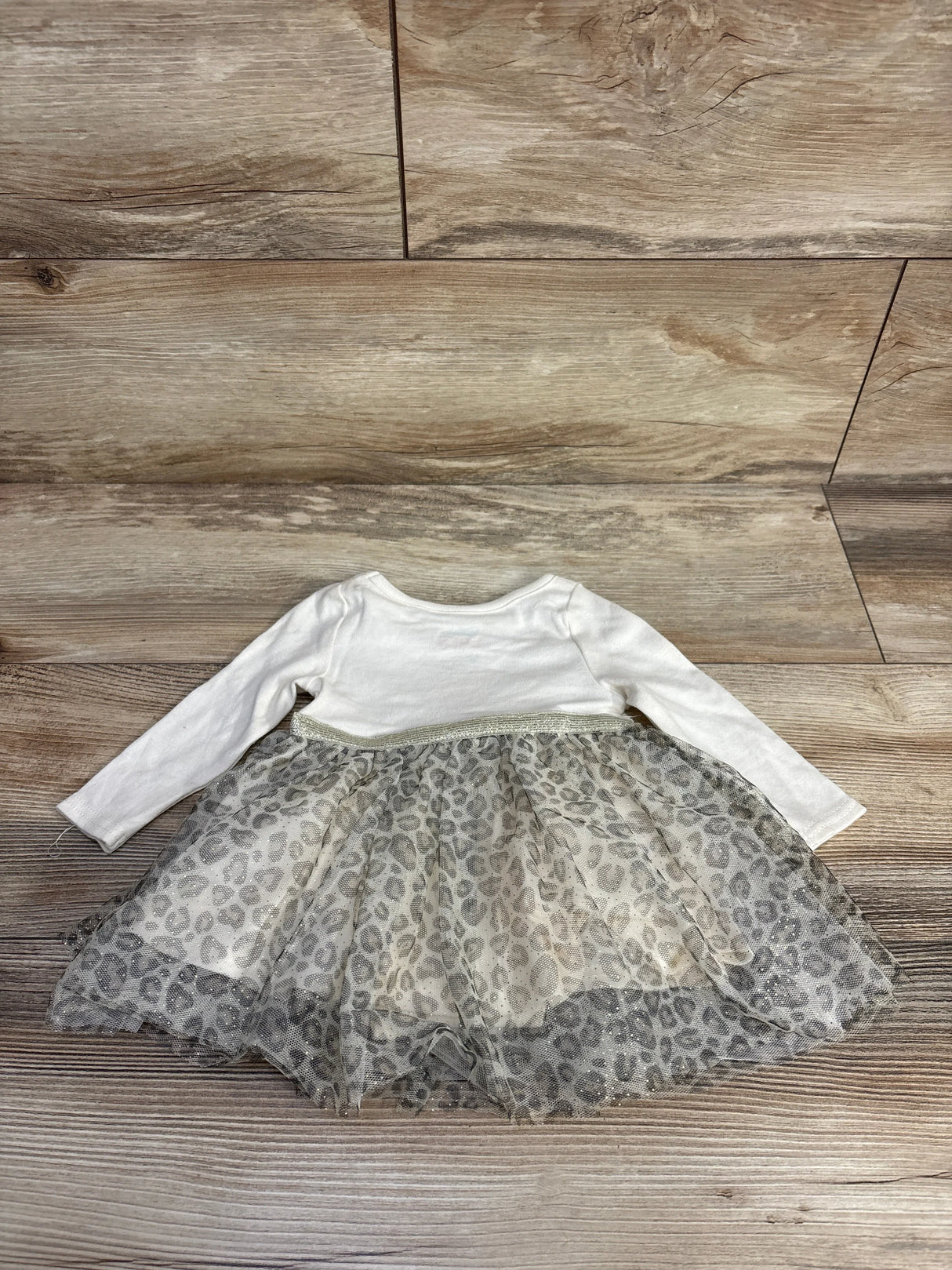 Flat lay of long sleeve baby dress with white knit top and gray leopard print tulle skirt on wood plank floor