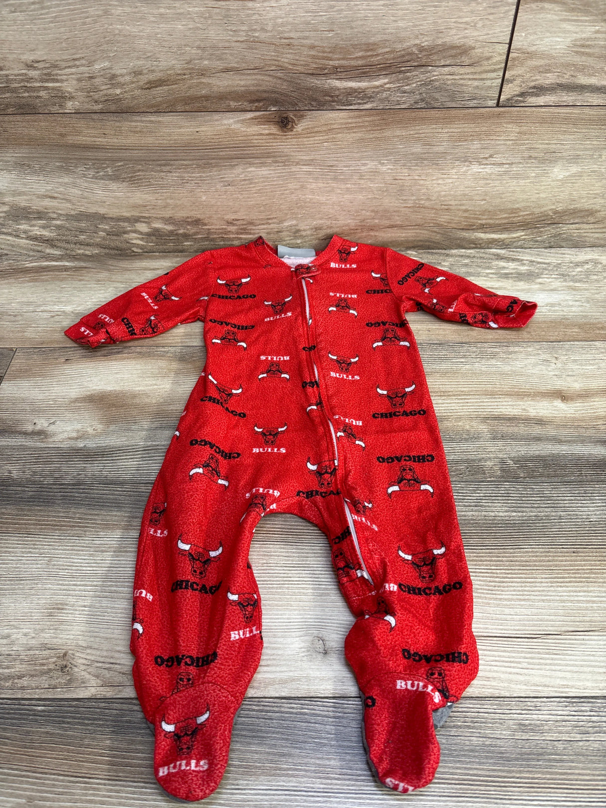 Red baby onesie with Chicago Bulls logo and text pattern laid on wooden floor