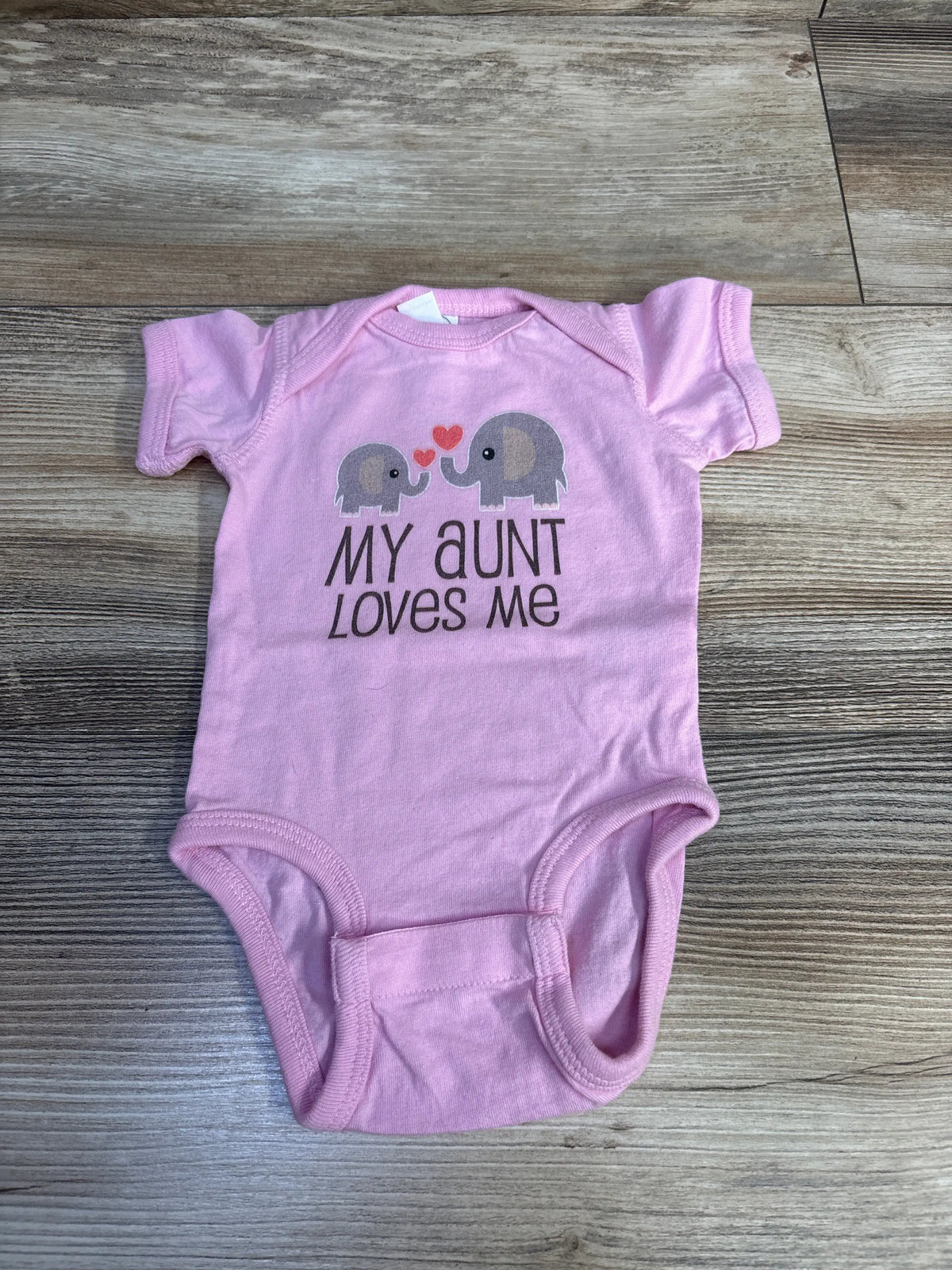 Front view of Rabbit Skins My Aunt Loves Me pink newborn bodysuit showcasing elephant graphic on wood-look background