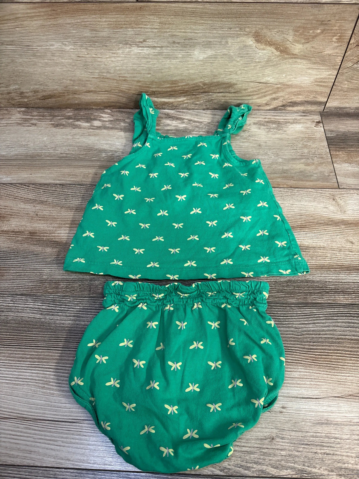 Top-down view of Carter’s two-piece smocked tank top and short set in green with a pale yellow pattern on a wood-grain background