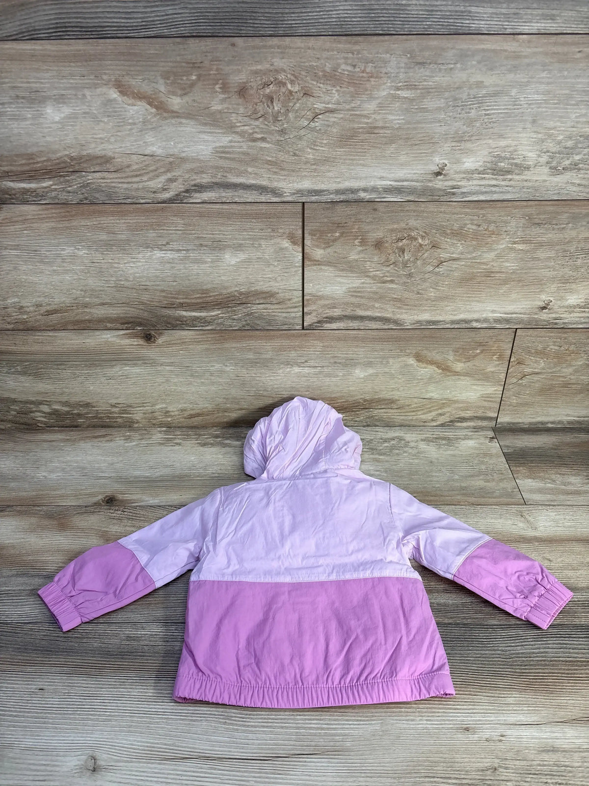 Back view of Cat and Jack windbreaker jacket size 12m with hood, elastic hem, and two-tone lilac and purple on wood floor