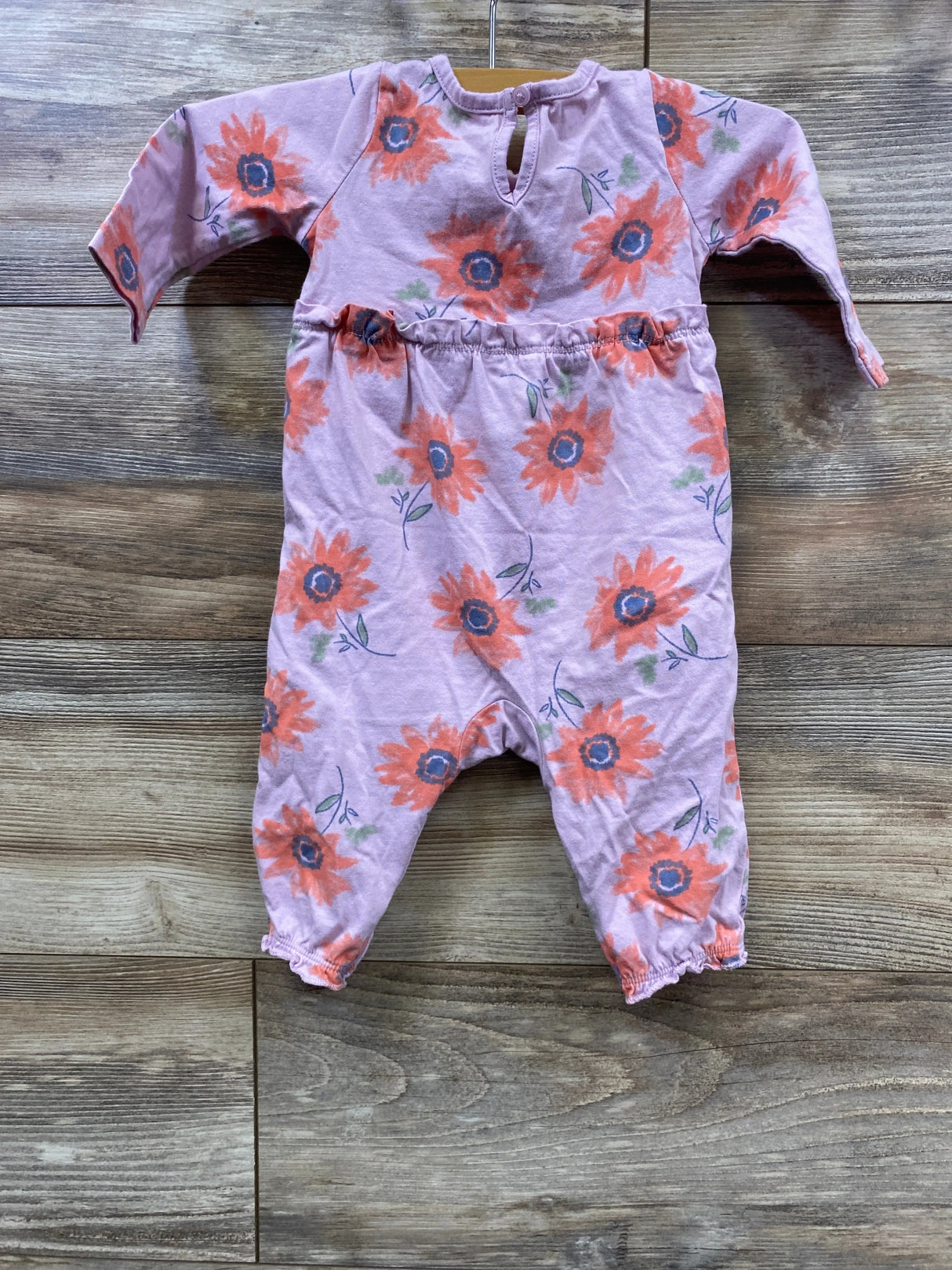 Pink baby romper with orange floral print and long sleeves on wooden floor