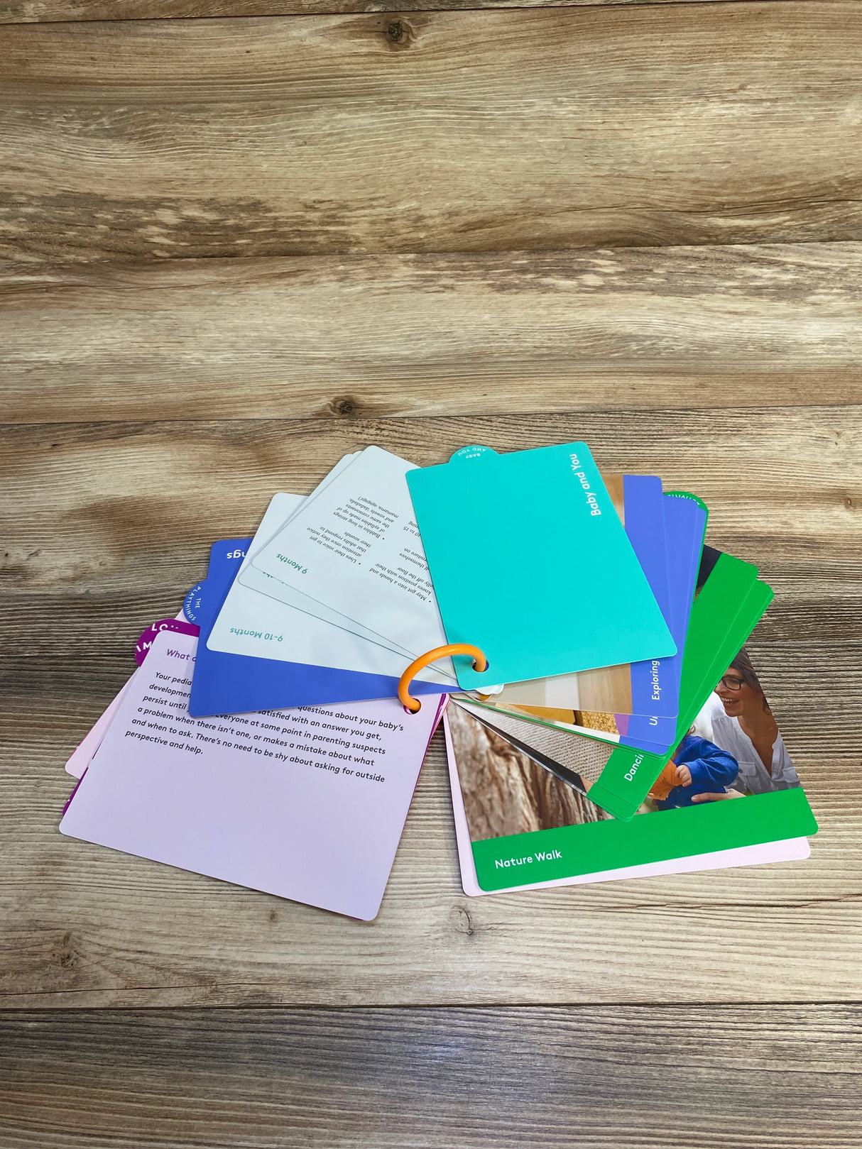 Colorful baby development activity cards on wooden surface, labeled with ages and topics