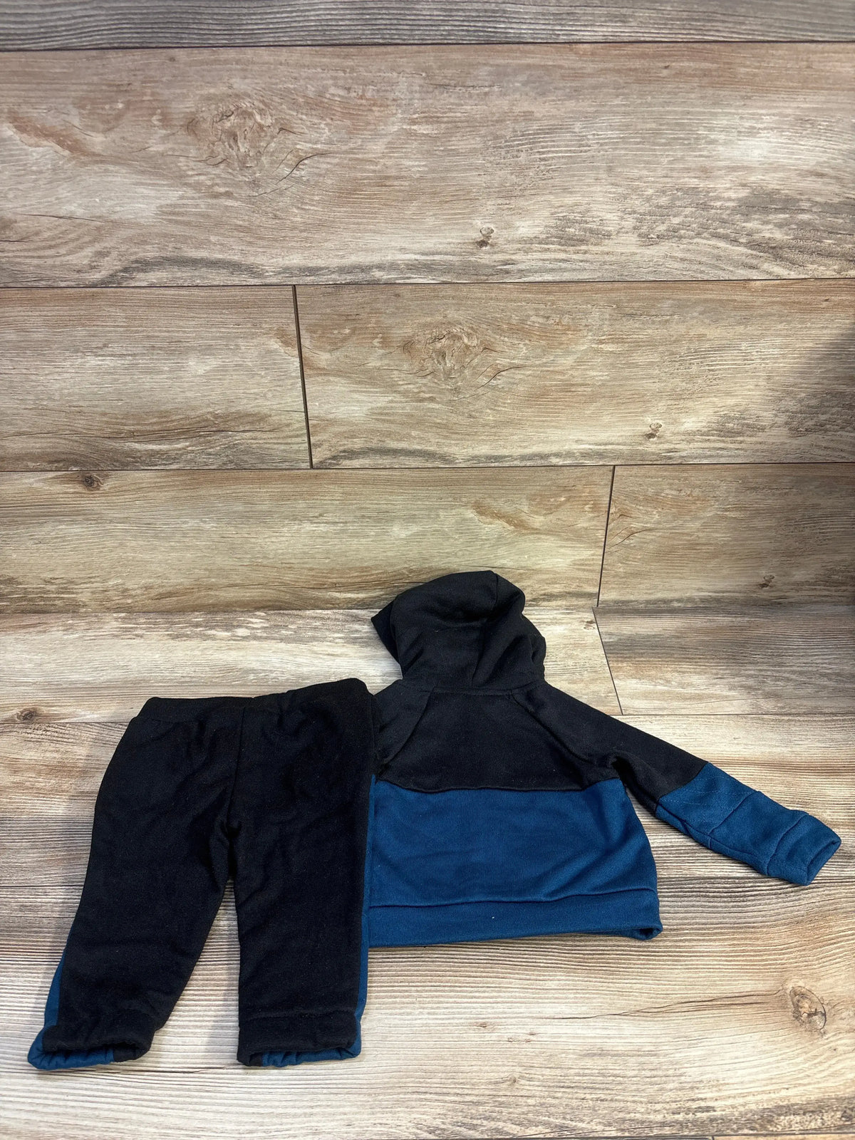 Flat lay of Ben Sherman baby zip-up hoodie and joggers showcasing black and blue colorblock design on wood plank background