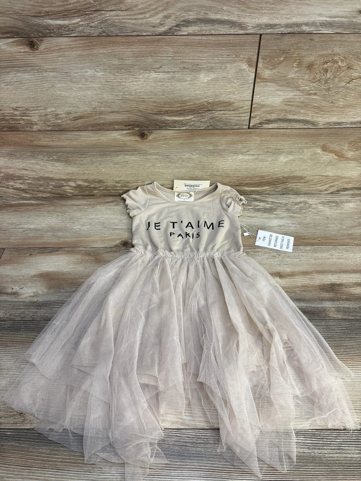 Flat lay of Mia Joy Feya toddler dress 3T with sand bodice reading Je T'aime Paris and layered tulle skirt on wood floor