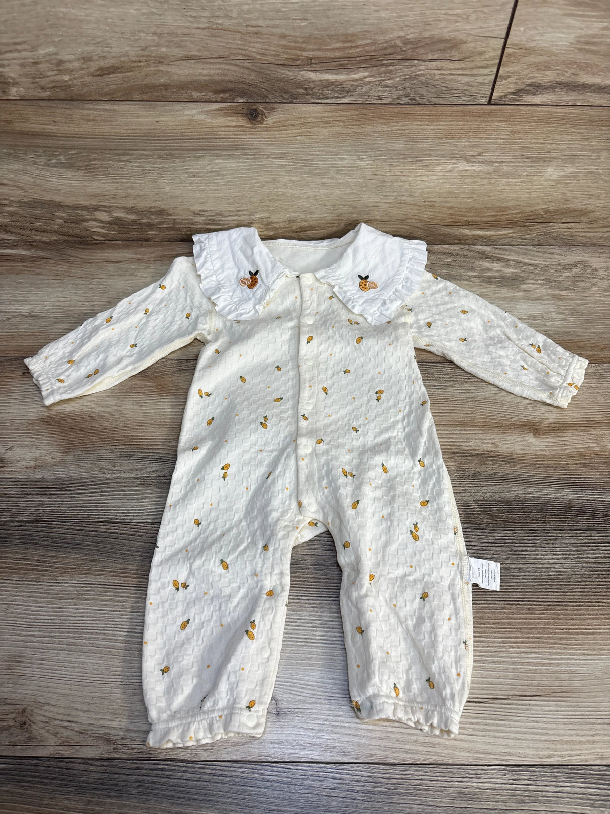 White baby romper with yellow fruit print and ruffled collar on wood floor