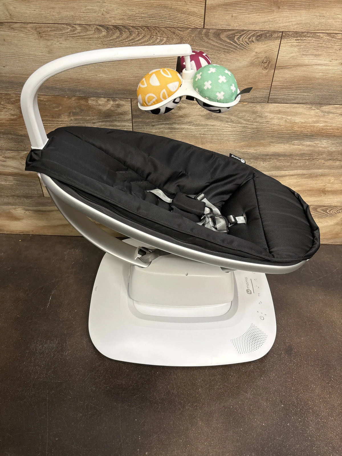 Angled view of 4moms mamaRoo Multi-Motion Baby Swing showcasing its black padded seat, harness, and toy bar on a white base