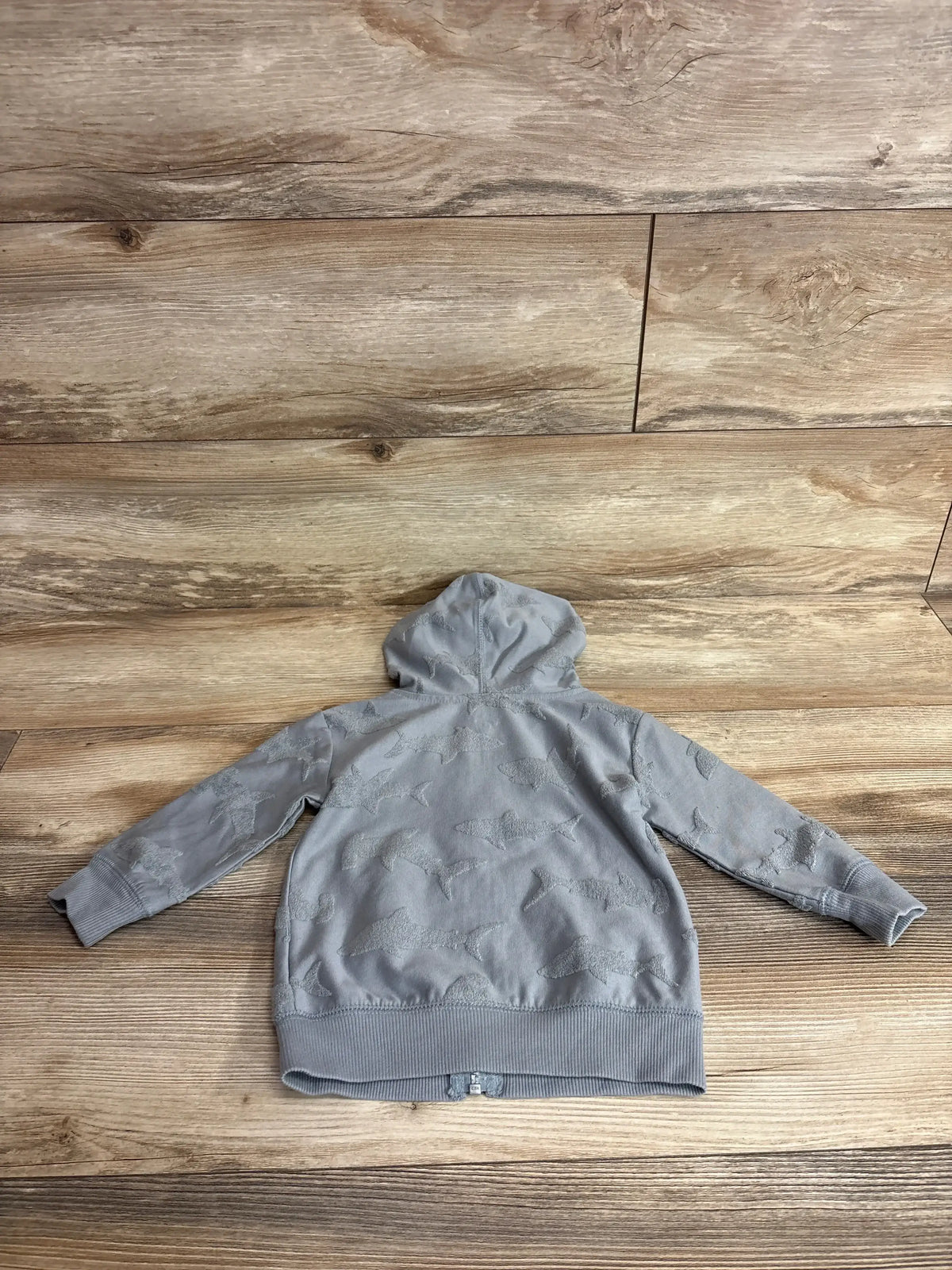 Back view of Jumping Beans hooded full-zip shark jacket, grey with raised shark pattern on light wood floor