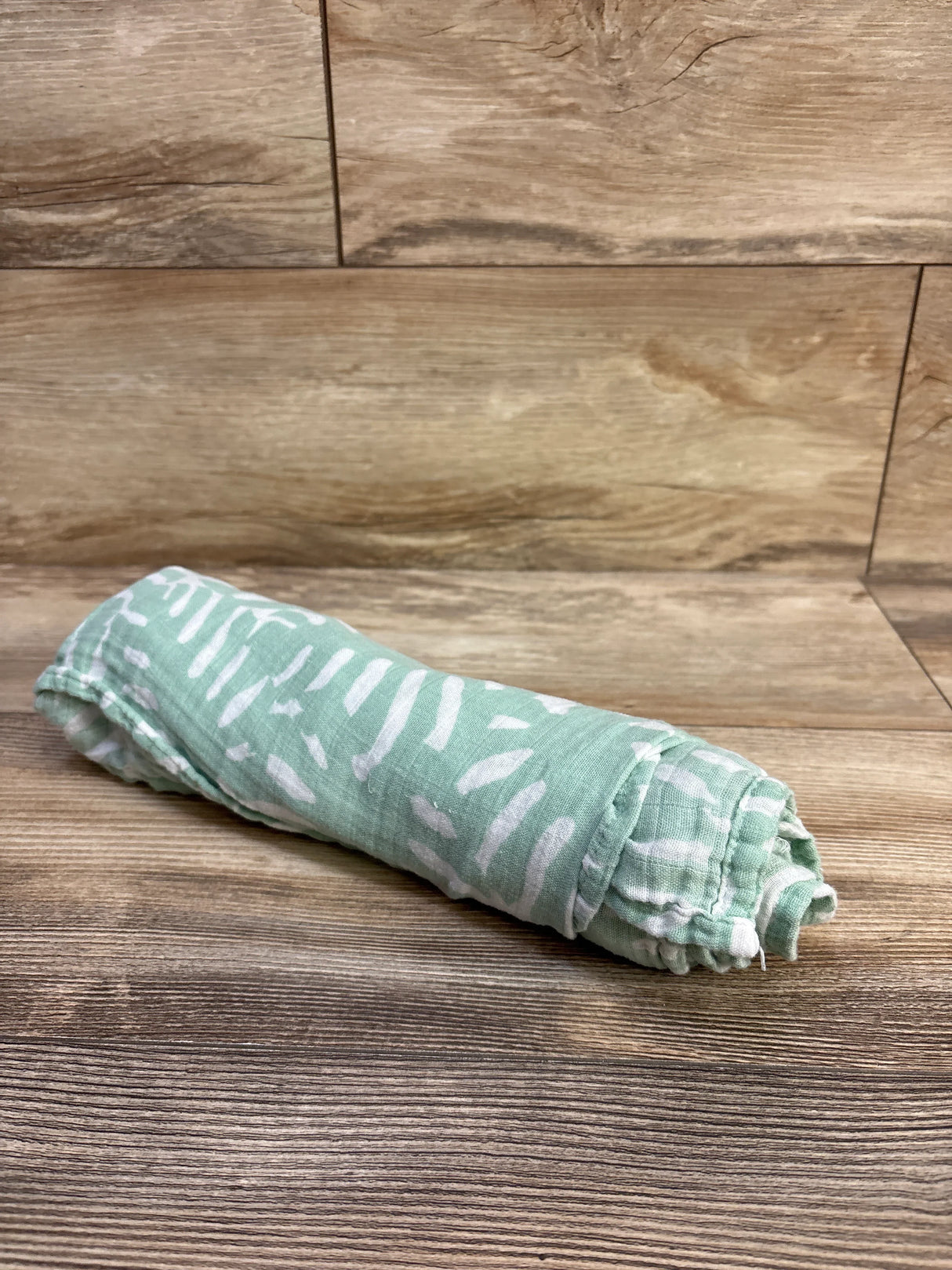 Rolled view of Momcozy bamboo swaddle blanket in green with white abstract pattern showing soft muslin texture on wood background