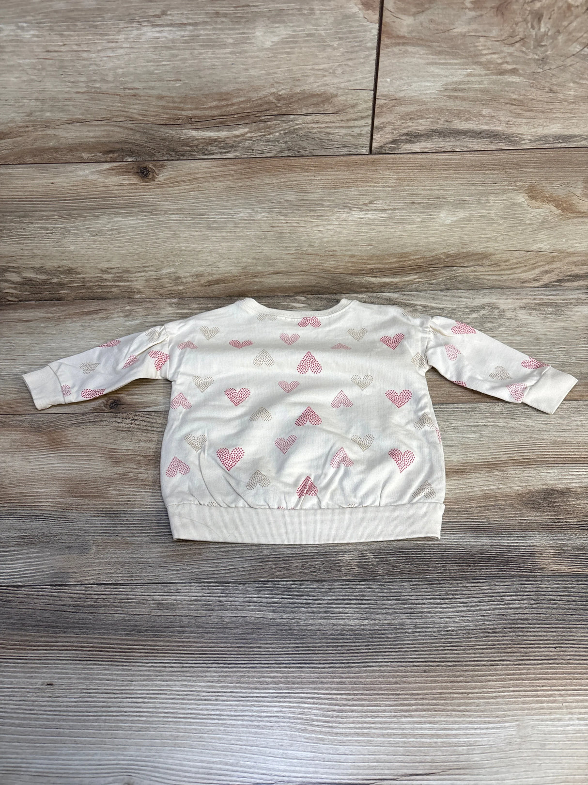 Long sleeve toddler shirt with pink and beige heart print on wood background