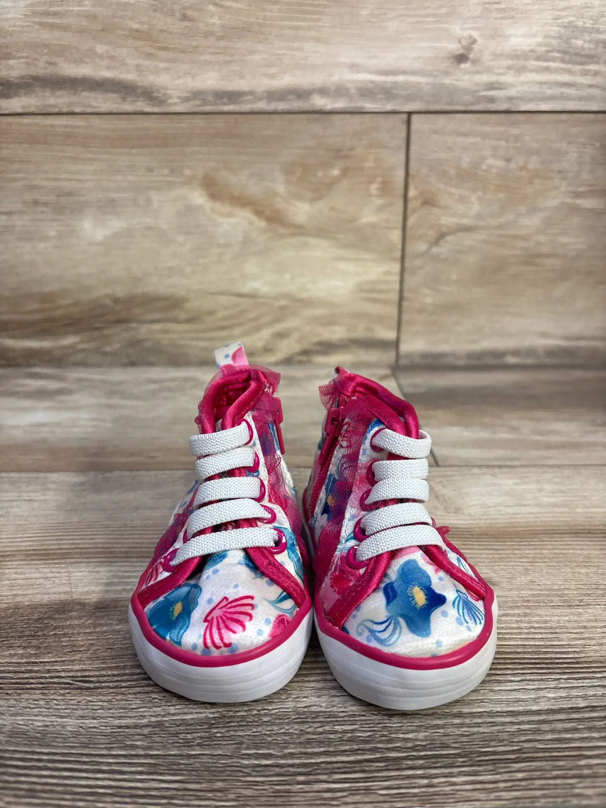 Front of toddler Disney floral high-top sneakers with pink trim, white laces and blue-pink flowers on white soles, wood floor
