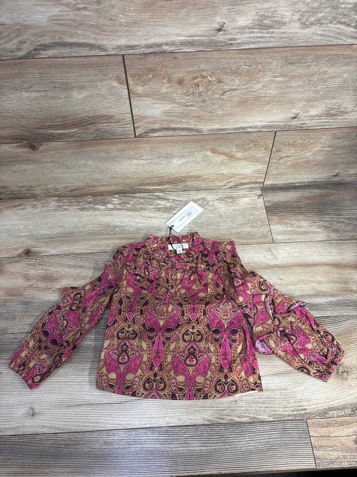 Pink and brown paisley patterned blouse with ruffle details and long sleeves on wood floor