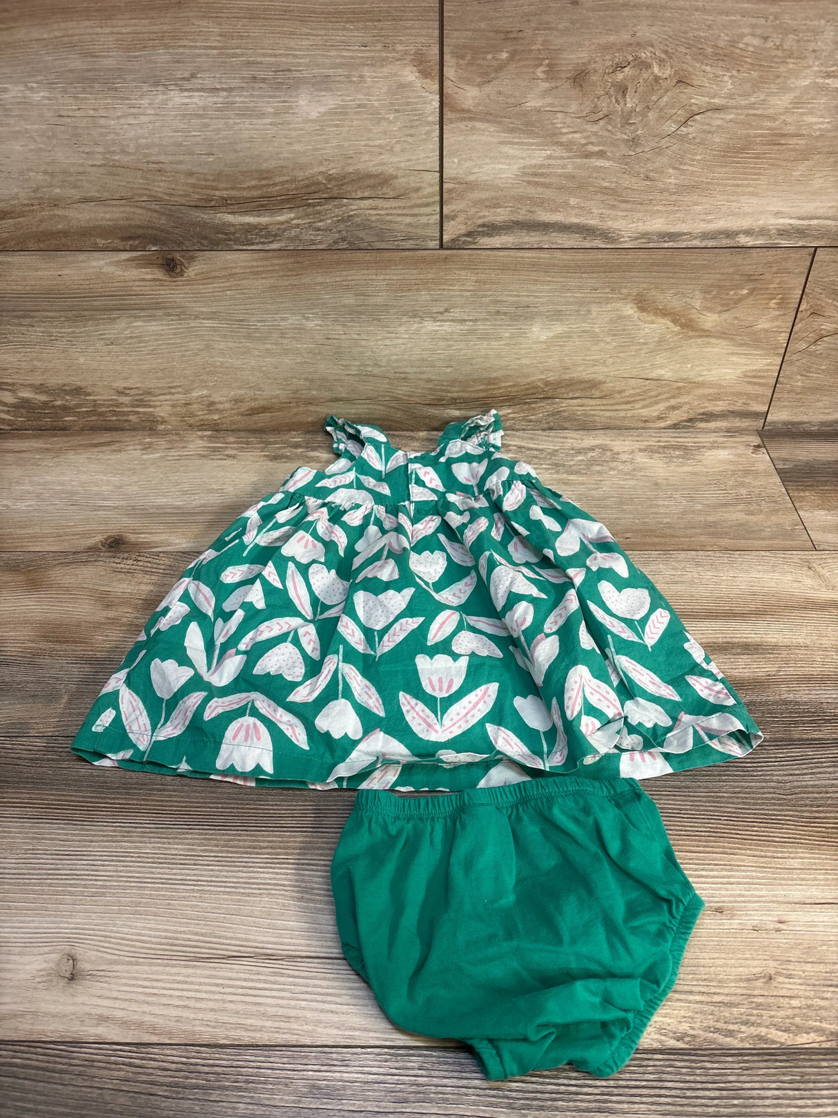 Flat lay of green girls dress and matching bloomers showing white and pale pink tulip print on wood background