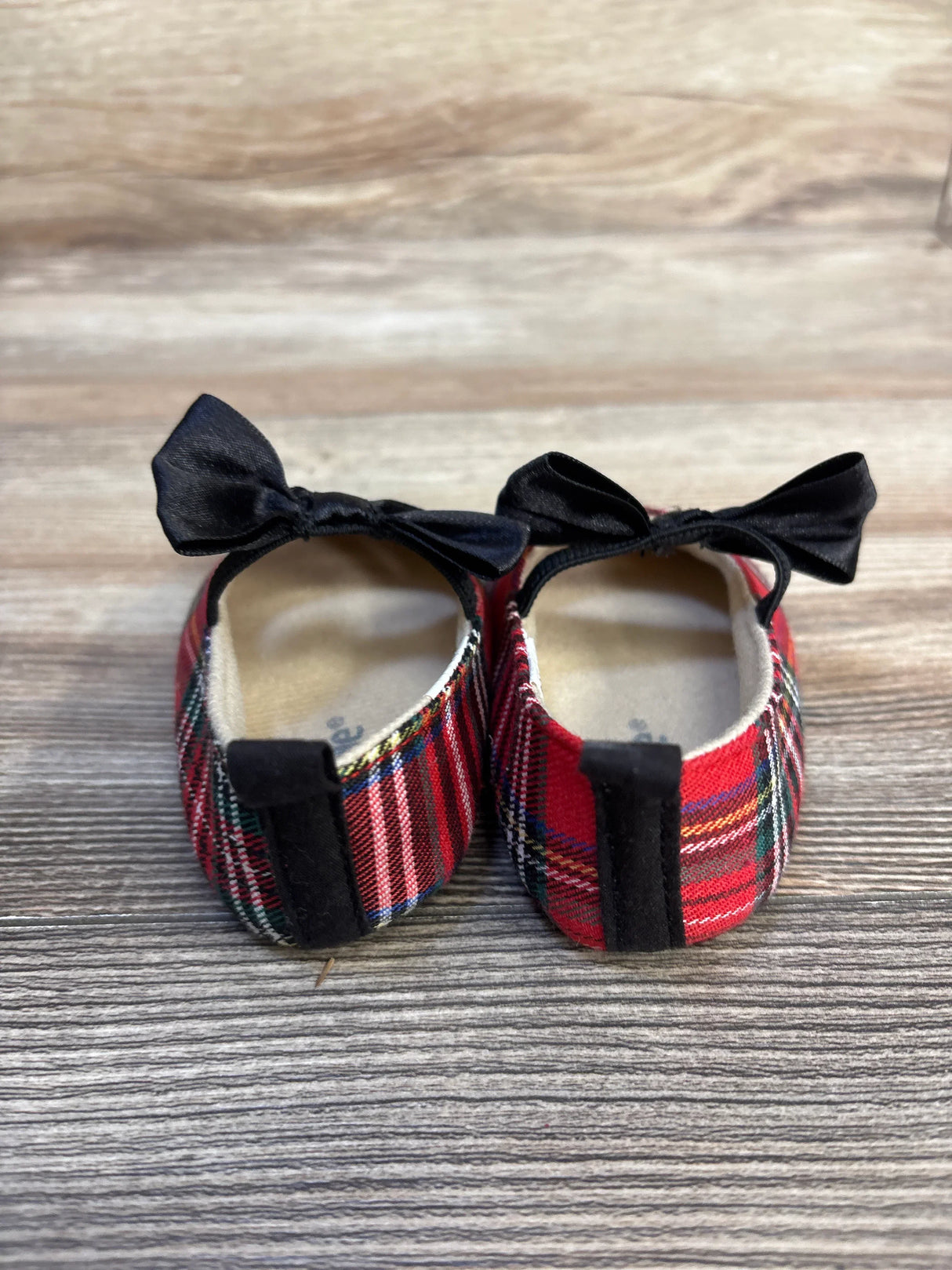Rear view of Little Me soft sole tartan Mary Jane flats with black satin bows, red plaid fabric and insole on wood background