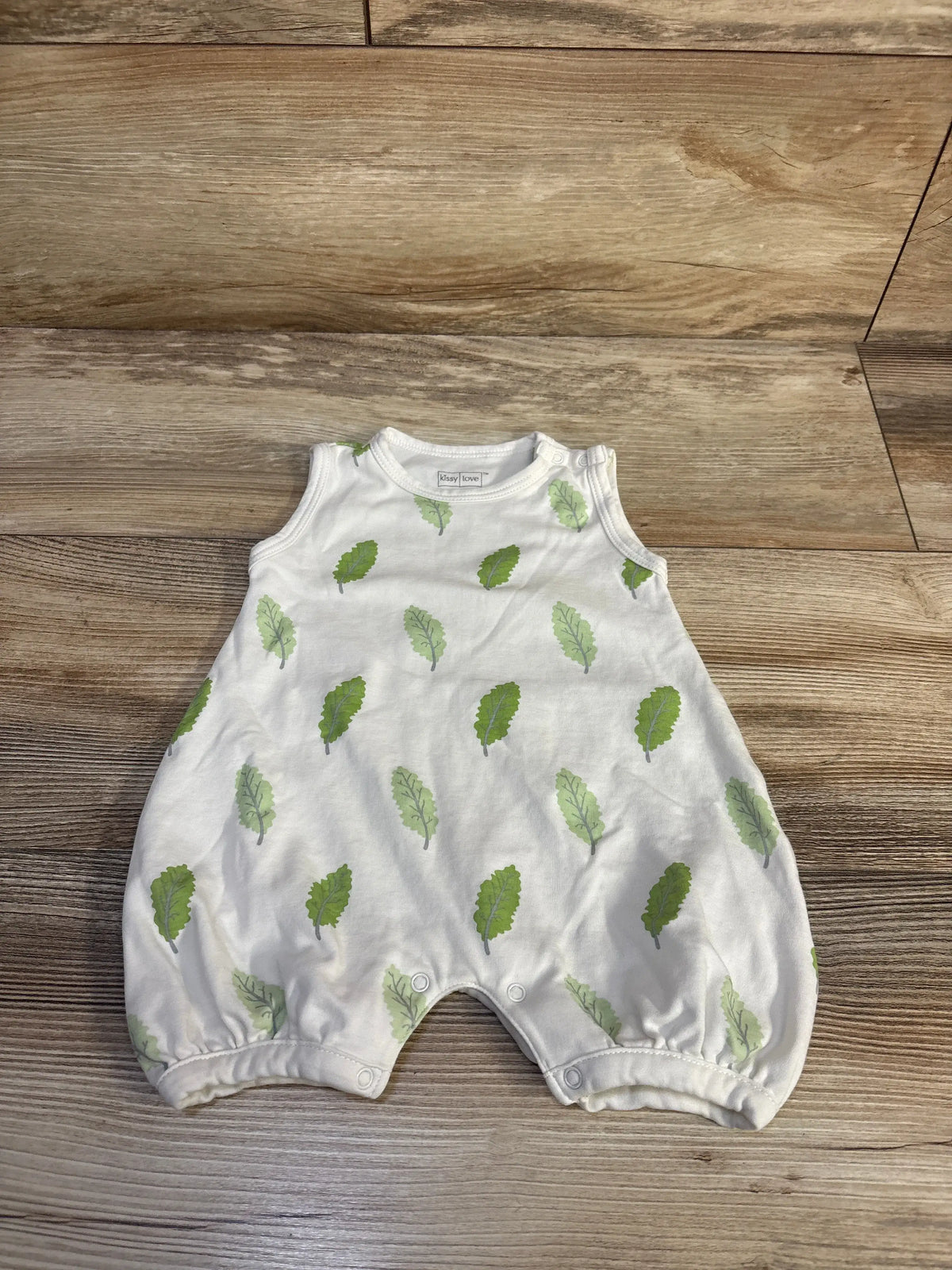 Front view of white Kissy Love leaf print shortie romper with short legs on a wood-grain background