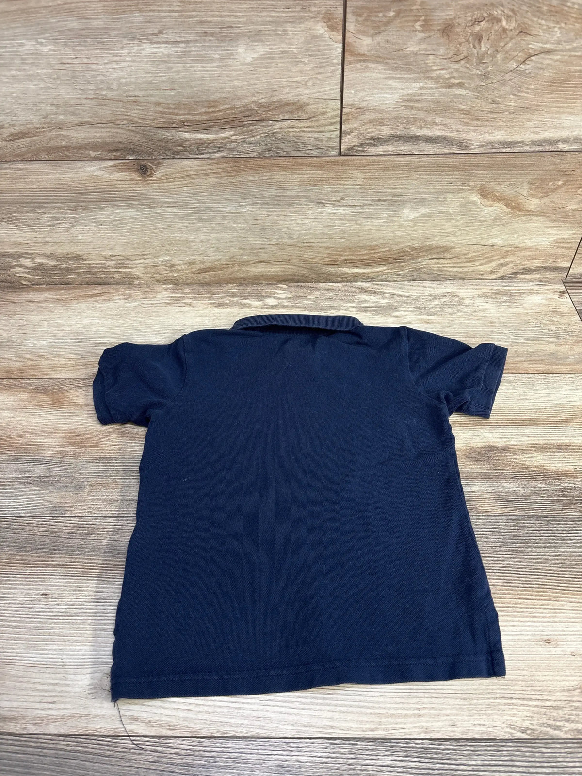 Back view of a navy blue short-sleeve polo shirt on wooden surface