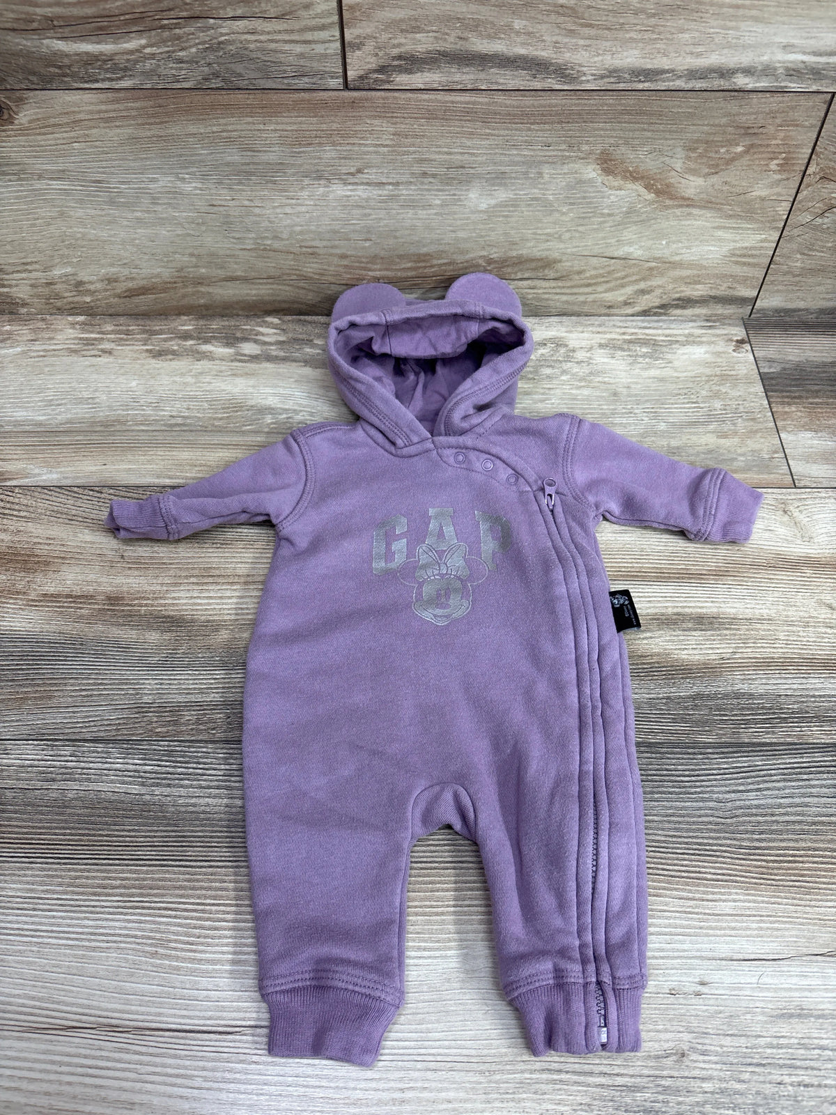 Front view of purple Baby Gap x Disney Minnie Mouse hooded coverall with ear-shaped hood and front zipper on wood floor