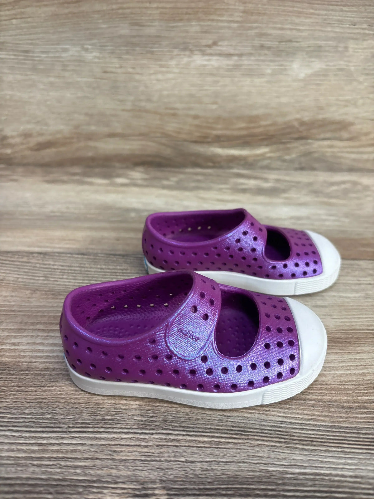 Side view of Native Jefferson Juniper shoes showing perforated purple upper, Mary Jane strap and white toe on wood background