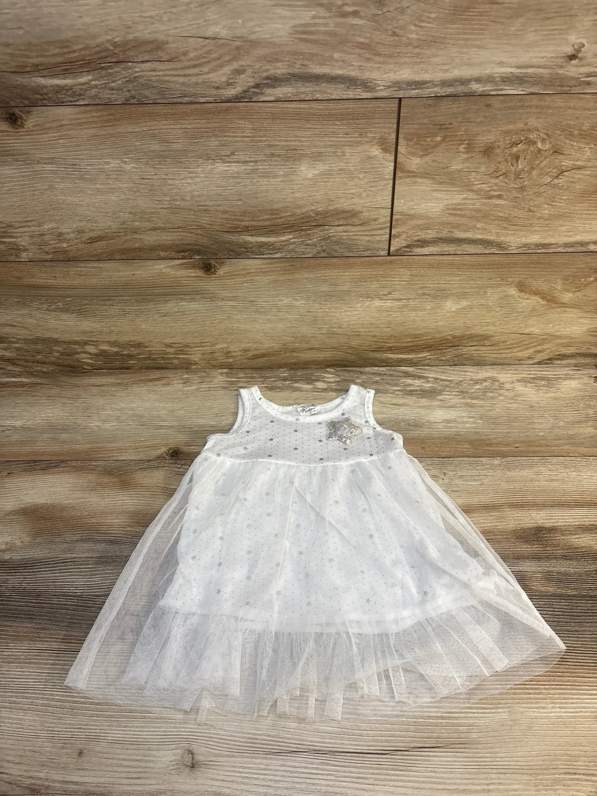 White toddler dress with tulle skirt and star embellishments on wooden floor