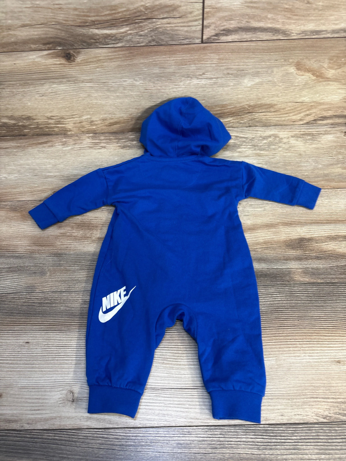 Blue hooded baby romper with white logo, long sleeves and legs, on wooden floor