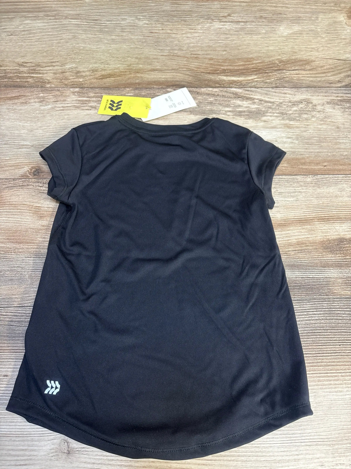 Back view of black All In Motion active shirt showing small reflective hem logo and yellow hangtag on wood floor
