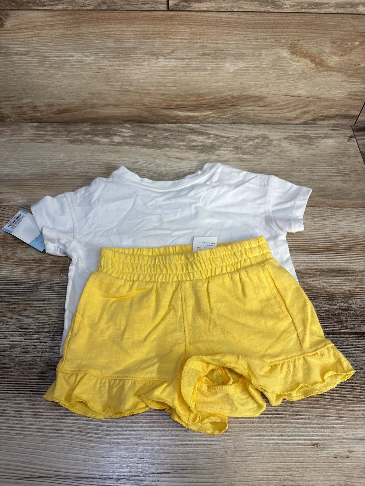 Front view of Cat & Jack Sun and Waves 2-piece set with white T-shirt and yellow ruffled shorts on wood