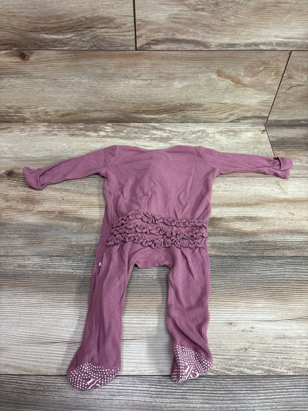 Front view of Caden Lane pink bamboo knit ruffle zipper footie showcasing ruffled waist and dotted foot grips on wood