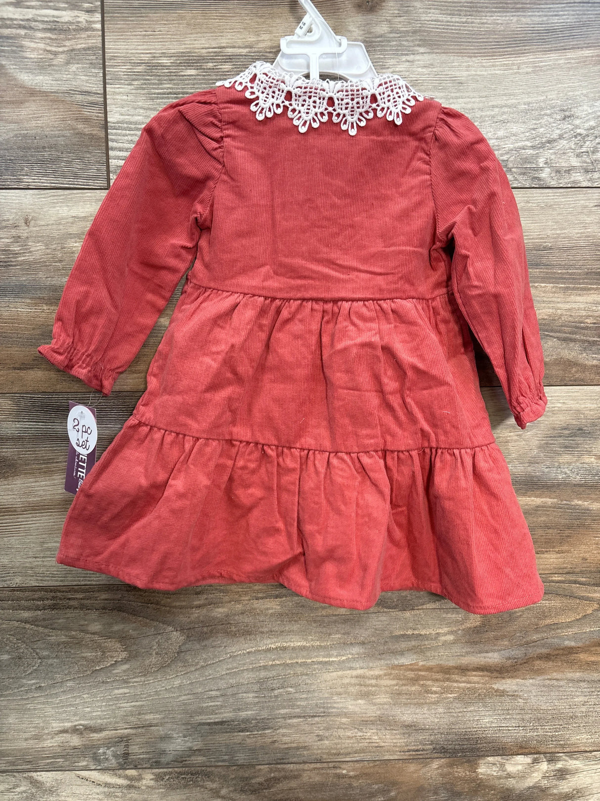 Rust red toddler dress with long sleeves and white lace collar hanging on wooden floor