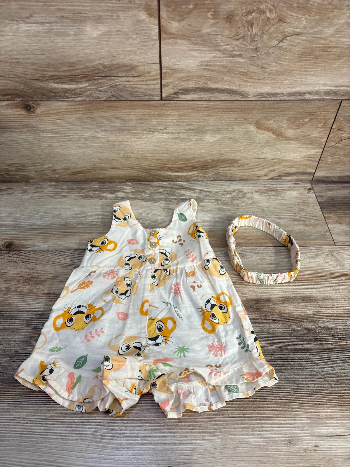 Front view of Disney Baby Lion King romper and headband set, ivory, size 3 to 6 months, with character print on wood floor
