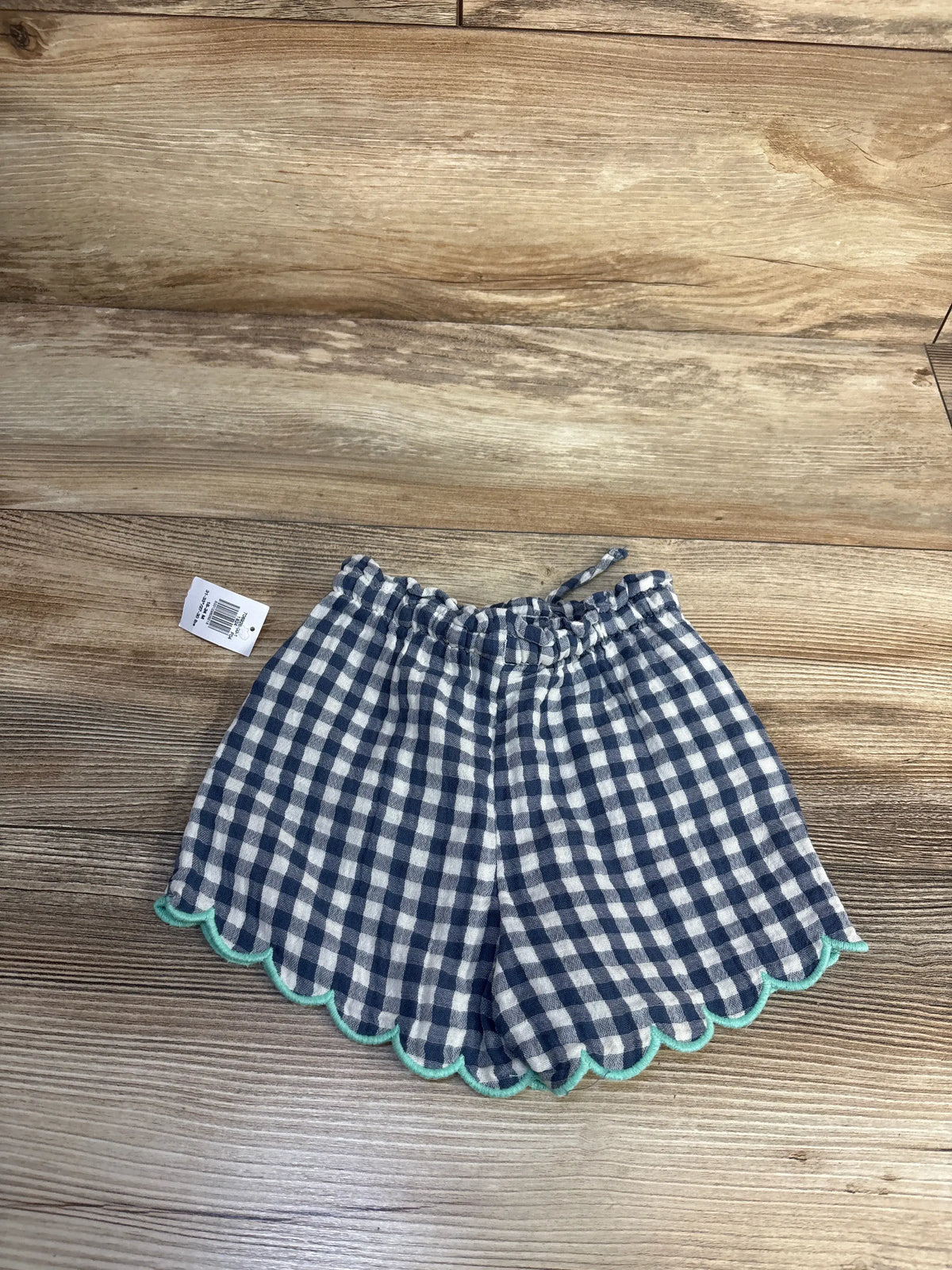 Top view of blue Old Navy gauze checkered toddler shorts showcasing scalloped trim and drawstring on wood background