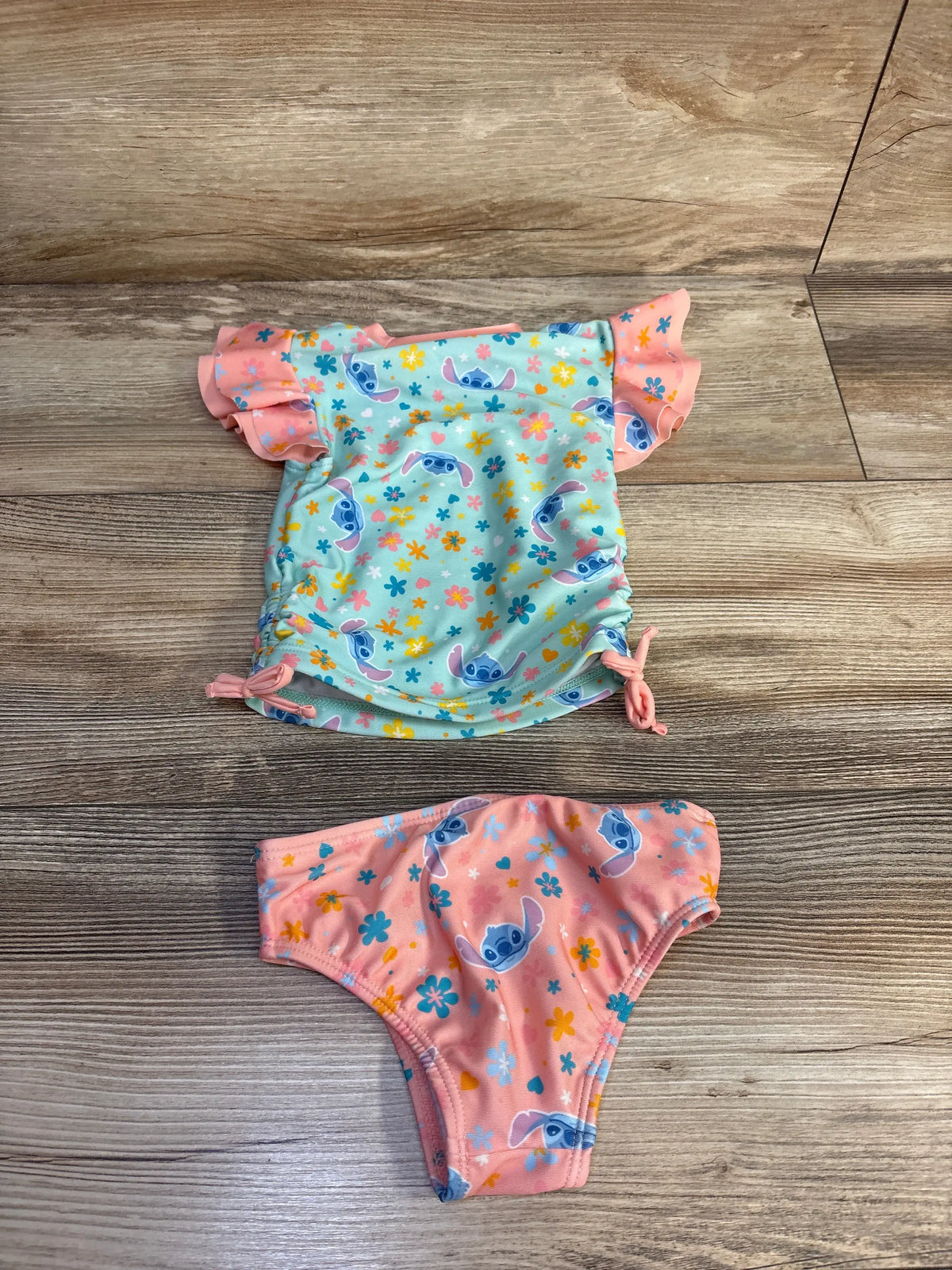 Flat lay of blue and pink Disney Stitch two-piece rash guard and bikini bottoms with character print and ruffled sleeves