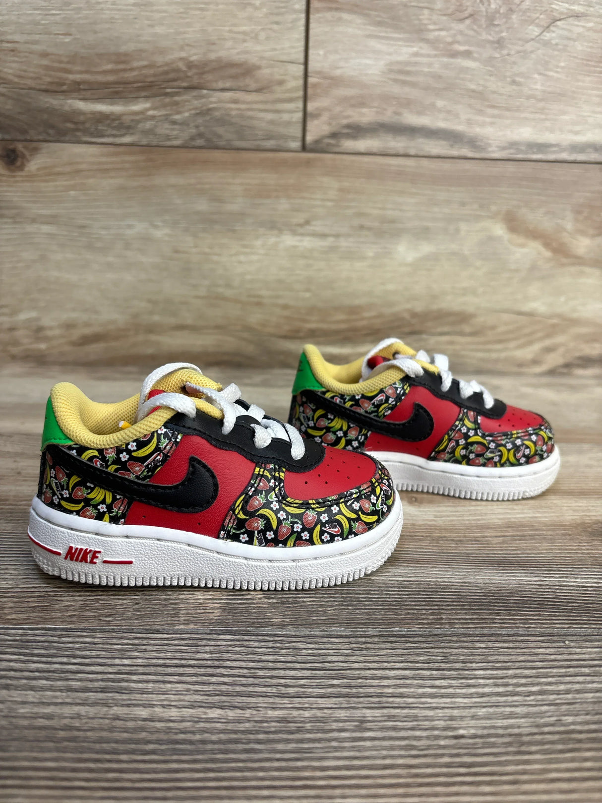 Kids Nike Air Force 1 sneakers with fruit print, red black white design, toddler shoes on wood floor