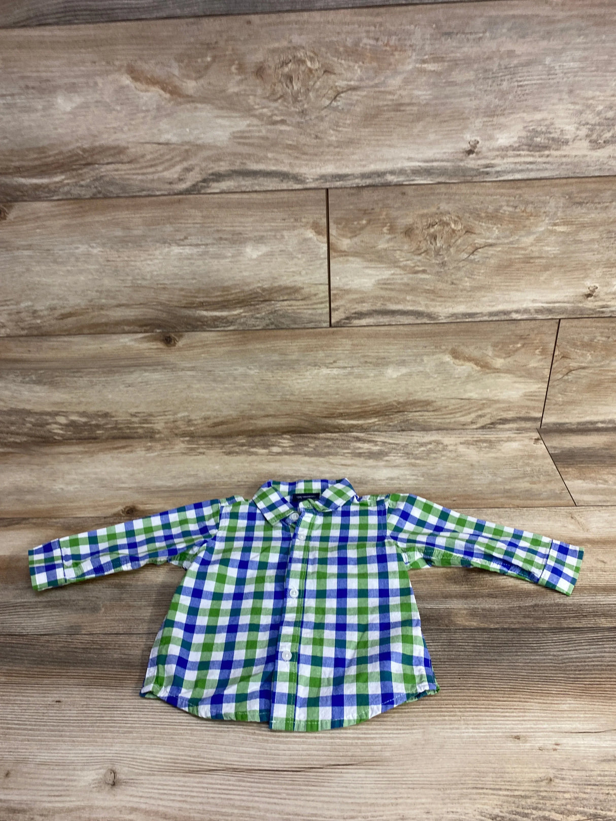 Green and blue plaid long sleeve button-up toddler shirt on wood background