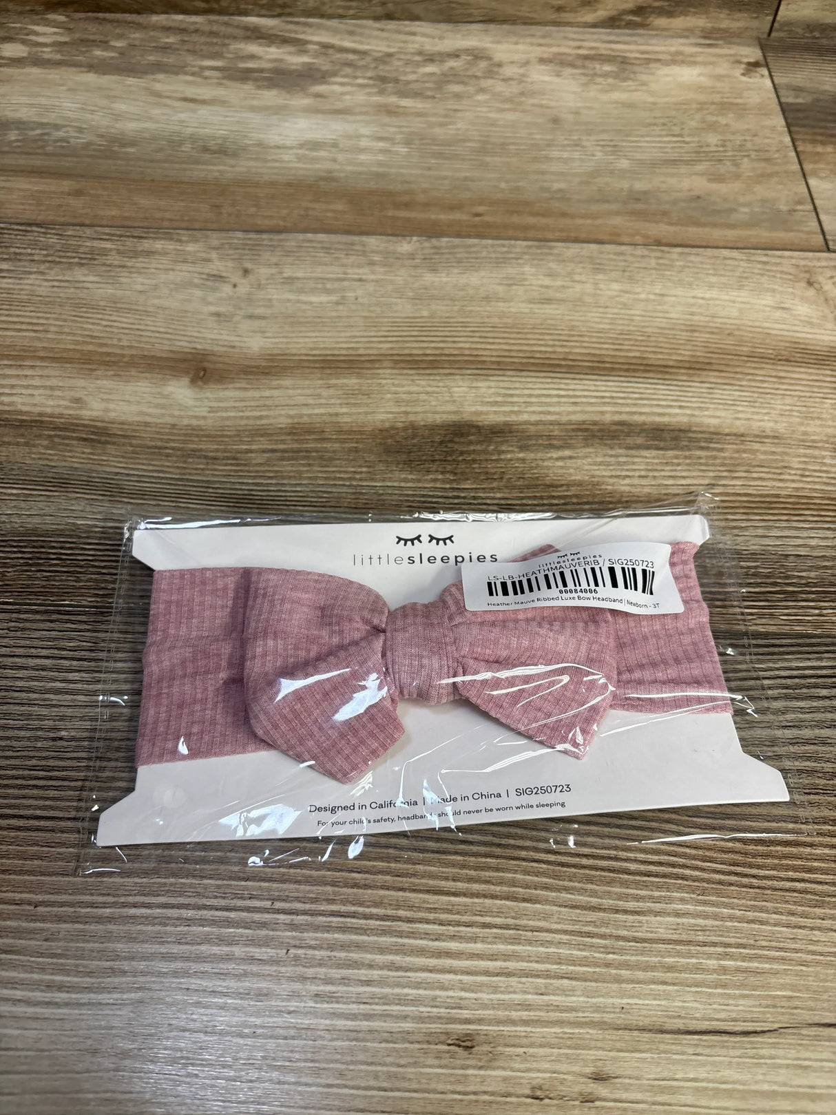 Front view of Little Sleepies mauve Ribbed Luxe bow headband with center knot on white card in plastic on wood background