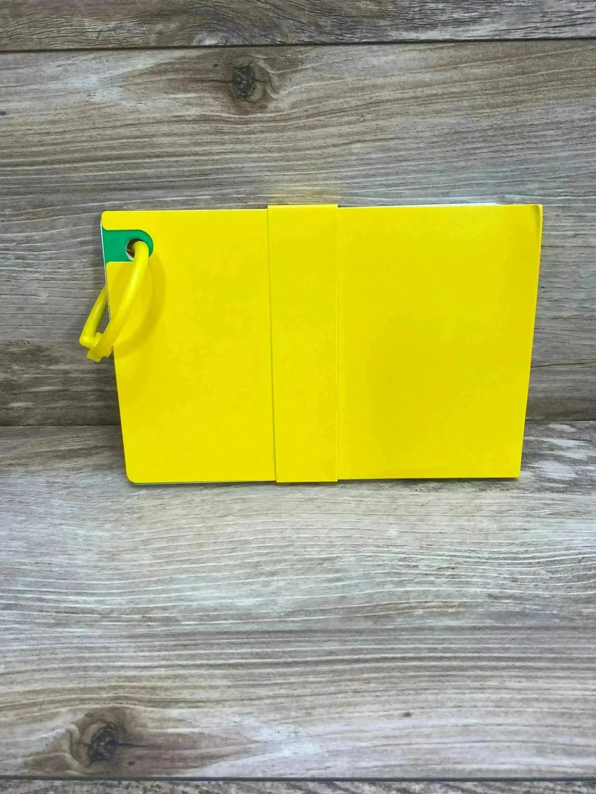Front view of Lovevery The Thinkers play guide (11–12 months) showcasing yellow board pages and attached yellow ring on wood background