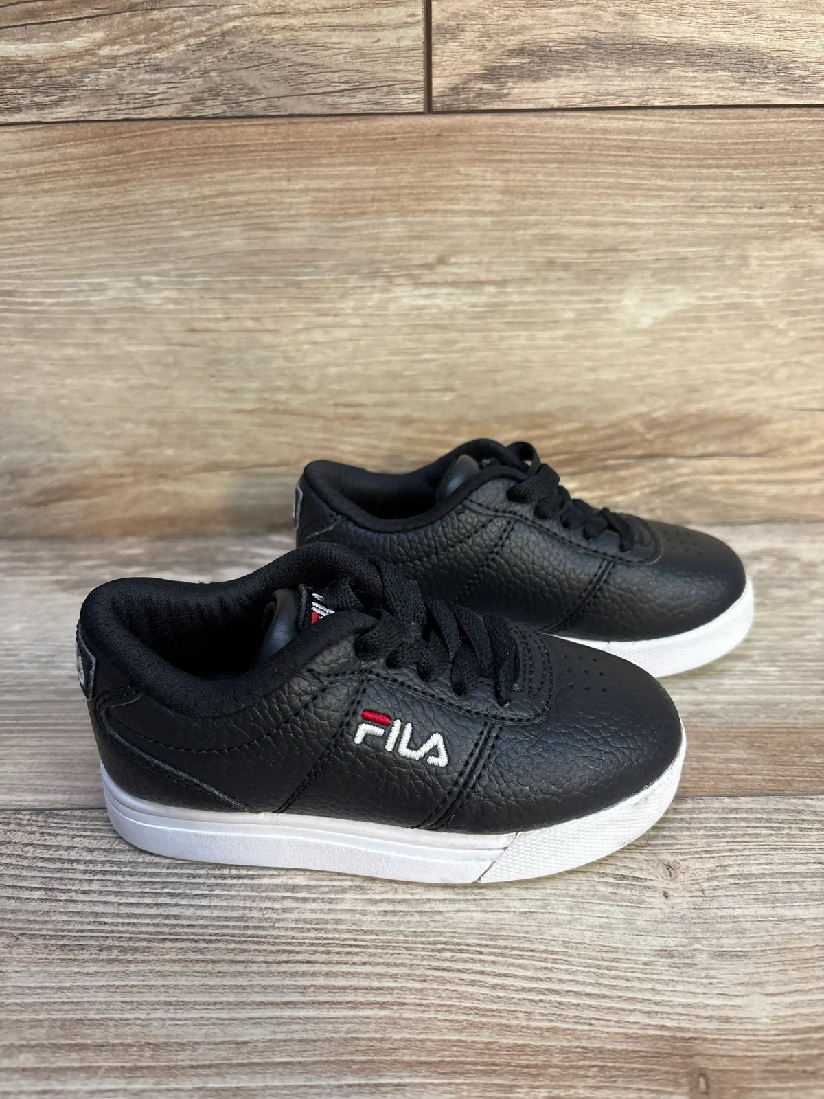 Pair of black Fila sneakers with white soles on wooden surface