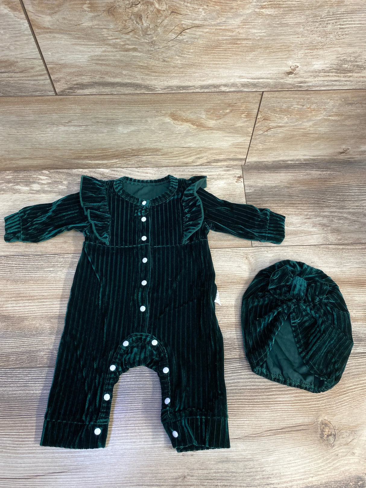 Dark green velvet baby romper and matching turban hat on wooden floor