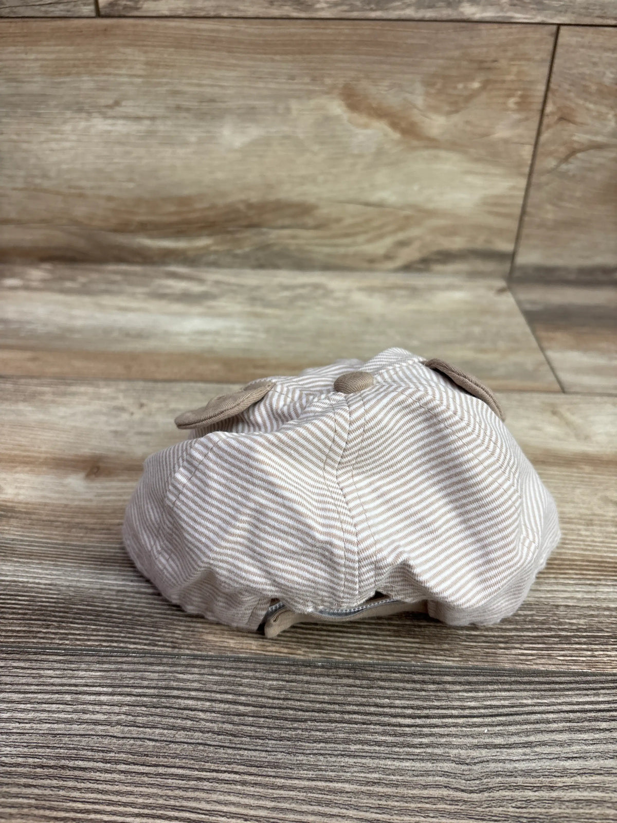 Rear view of Wander & Dreams infant bear hat in beige showcasing bear ears and striped fabric on a wood-grain floor