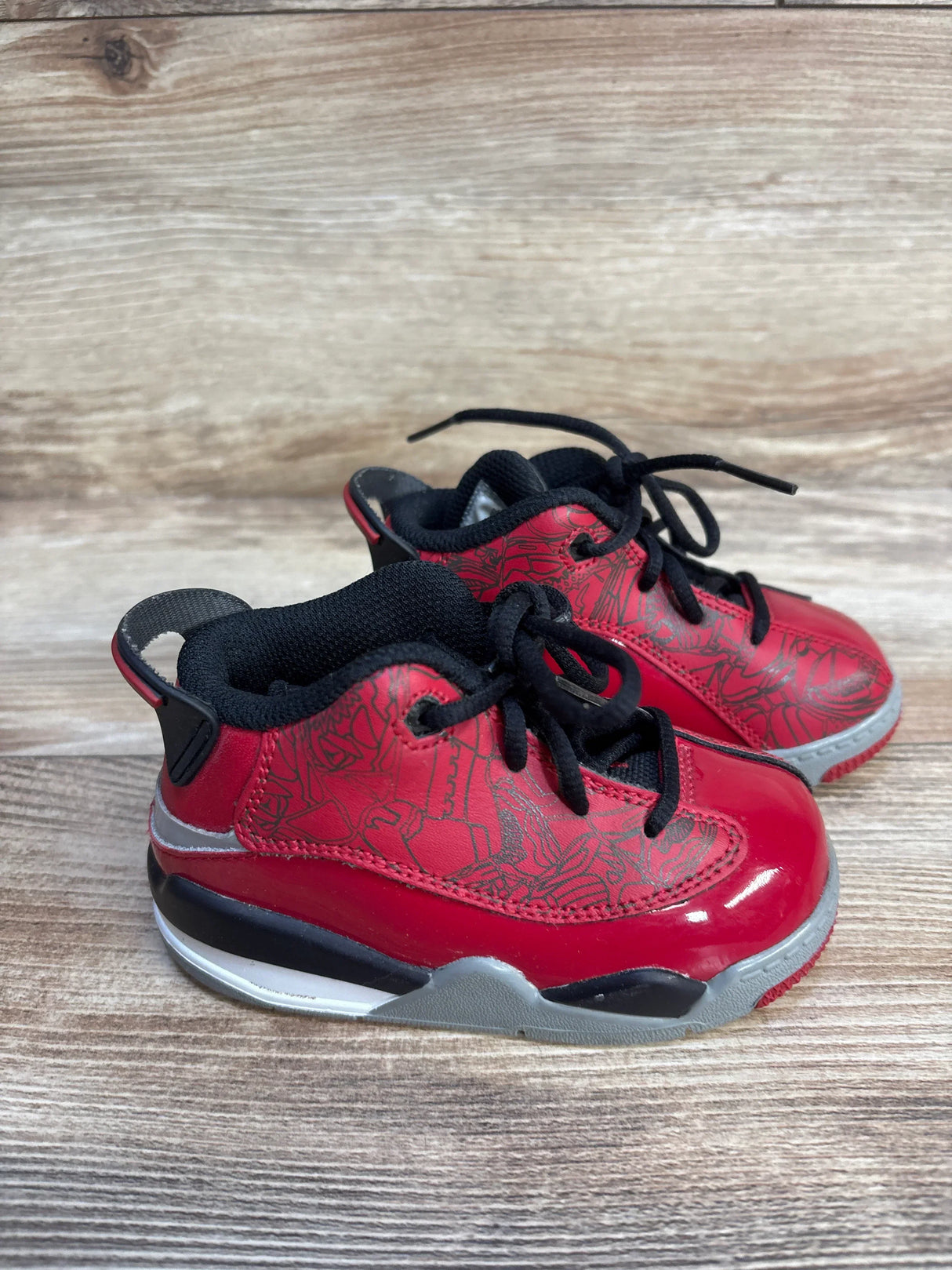 Red and black toddler sneakers with graphic pattern, placed on wooden background