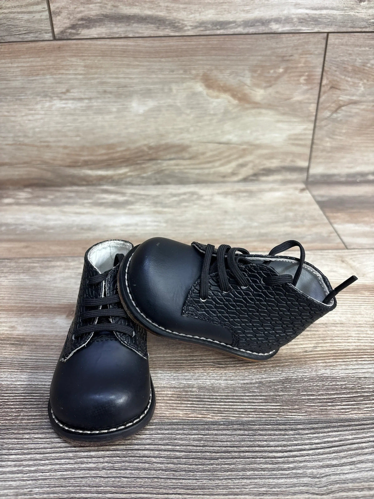 Black baby lace-up shoes with textured sides on wooden background, toddler footwear