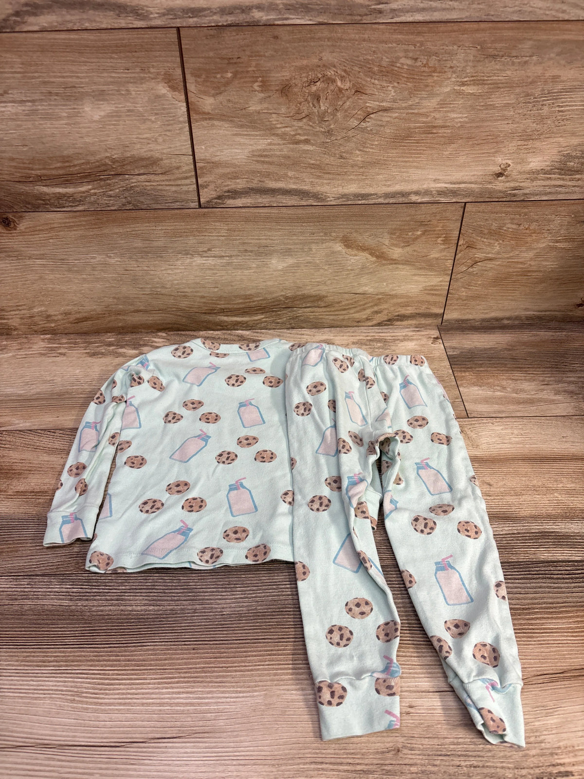 Flat lay of Monica and Andy 2pc Cookies and Milk pajama set in mint, size 3T, with cookie and milk bottle print on wood